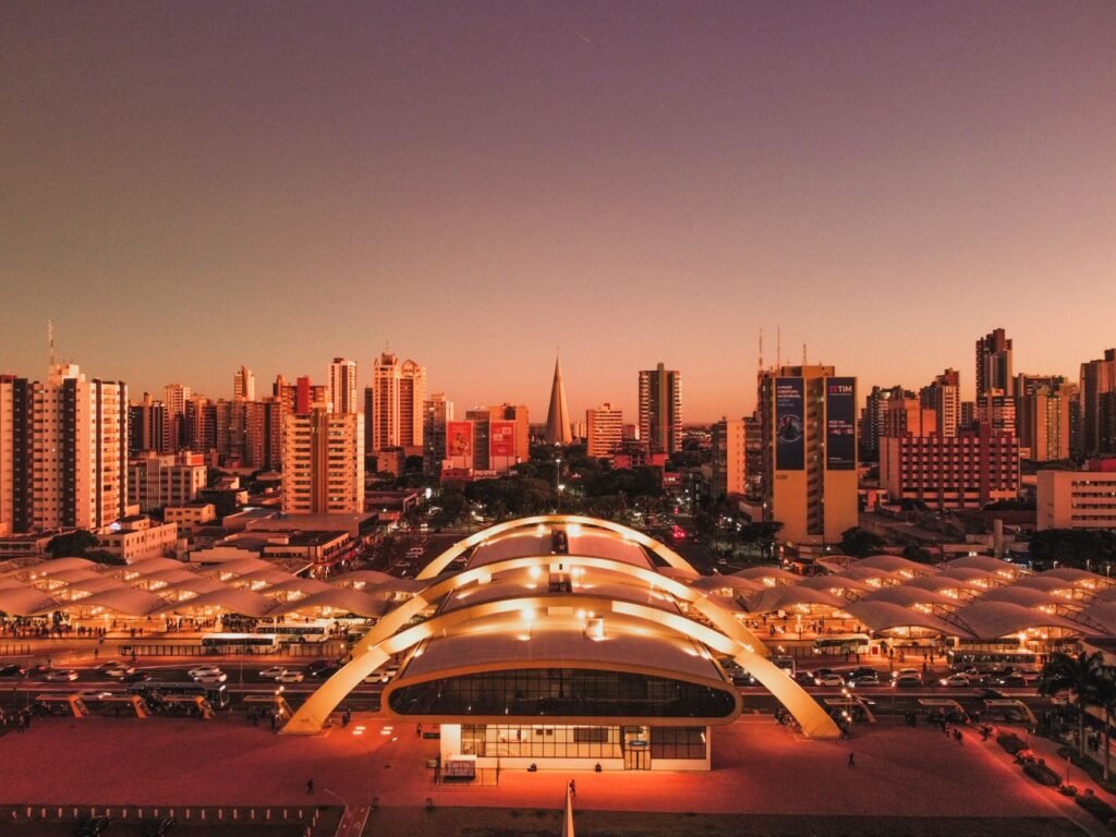 Vista aérea de cidade paranaense ao entardecer, com terminal de ônibus iluminado